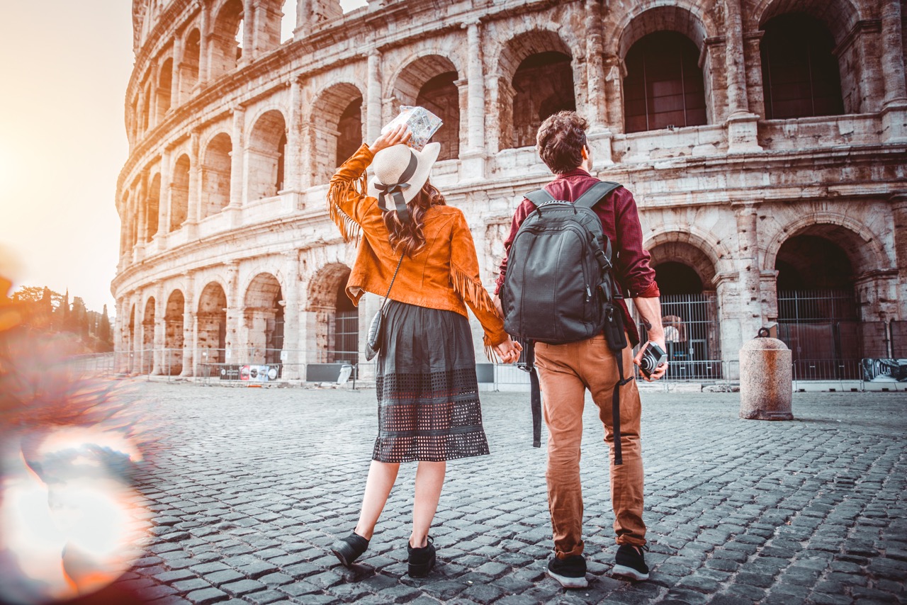 A couple joyfully taking a selfie in front of the Colosseum in Rome, Italy.